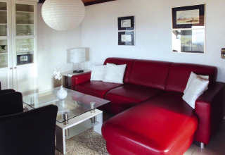 Sala moderna con sofá de cuero rojo, mesa de cristal y cojines blancos en Holiday village Öfingen, Alemania.