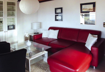 Modern living room with red leather sofa, glass table, and white pillows at Holiday village Öfingen, Germany.