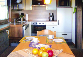 Zona cucina e pranzo accogliente in uno chalet con fruttiera e piatti apparecchiati sul tavolo.