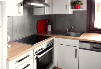 Cucina moderna in chalet con mobili bianchi, piano in legno, fornello, lavello e finestra a Öfingen.