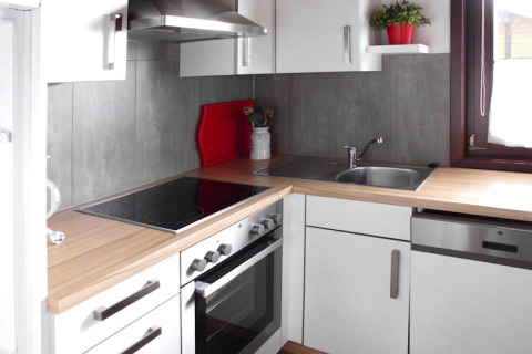 Cucina moderna in chalet con mobili bianchi, piano in legno, fornello, lavello e finestra a Öfingen.