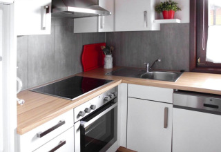 Moderne chaletkeuken met witte kasten, houten werkblad, oven en ruim raam in Öfingen, Duitsland.