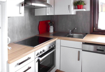 Modern chalet kitchen with white cabinets, wood countertop, stove, sink, and window in Öfingen, Germany.
