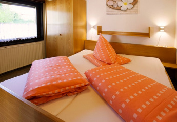 Chambre du chalet Holiday village Öfingen, Allemagne, avec lit double, linge orange et mobilier moderne.