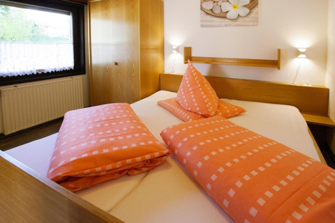 Dormitorio en la cabaña Holiday village Öfingen, Alemania, con ropa de cama naranja y muebles de madera.