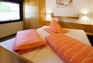 Camera da letto nel chalet Holiday village Öfingen, Germania, con letto matrimoniale e biancheria arancione.