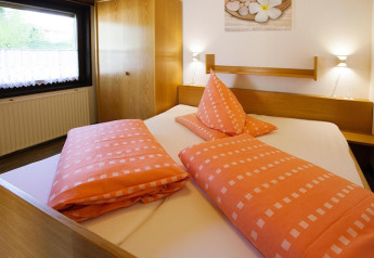 Slaapkamer in chalet Holiday village Öfingen, Duitsland, met oranje beddengoed en houten meubilair.