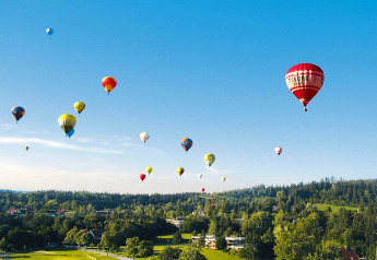Mongolfiere colorate volano sopra colline e alberi verdi presso Holiday village Öfingen in Germania.