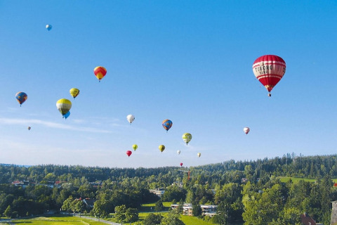 Kleurrijke luchtballonnen zweven boven groene heuvels en bomen bij vakantiepark Öfingen, Duitsland.