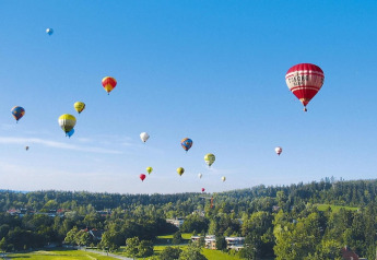 Colorful hot air balloons float over green hills and trees at Holiday village Öfingen in Germany.