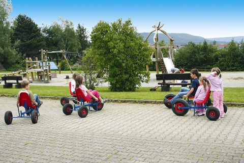 Children ride pedal go-karts near a playground at Holiday village «Öfingen - 68 sqm Type C Sioux» in Germany.