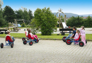 Children ride pedal go-karts near a playground at Holiday village «Öfingen - 68 sqm Type C Sioux» in Germany.