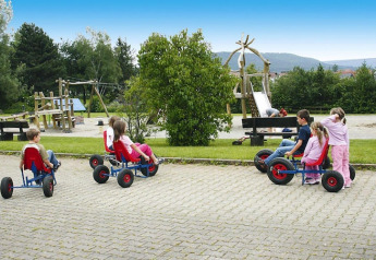 Bambini giocano con go-kart a pedali accanto al parco giochi al Holiday village «Öfingen - 68 sqm Type C Sioux» in Germania.