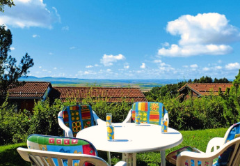 Buitentafel met kleurrijke stoelen en uitzicht op vakantiehuisjes en landschap bij vakantiepark Öfingen.