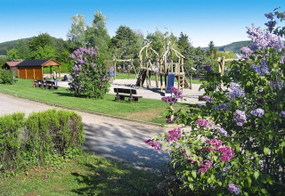 Speeltuin met houten speeltoestellen, banken en bloeiende struiken in vakantiedorp Öfingen, Duitsland.