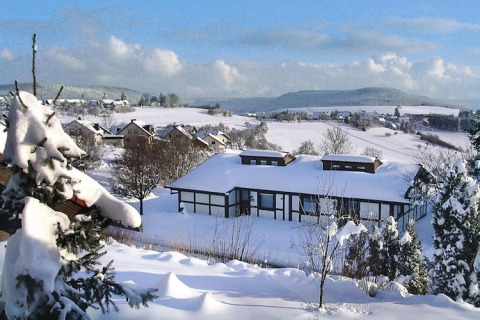 Paisaje nevado con pueblo y chalet Holiday village Öfingen, Alemania, rodeado de colinas durante el invierno.