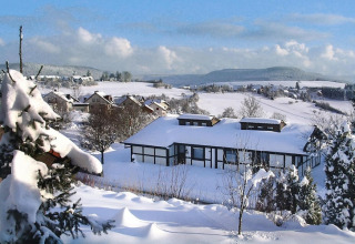 Paisaje nevado con pueblo y chalet Holiday village Öfingen, Alemania, rodeado de colinas durante el invierno.