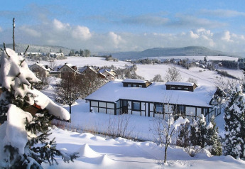 Sneeuwlandschap met chalets en dorp bij Holiday village Öfingen, Duitsland, winters aanzicht en heuvels.