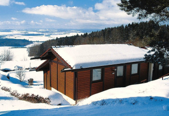 Chalet coperto di neve al villaggio Holiday Öfingen, Germania, con paesaggio invernale e foresta.