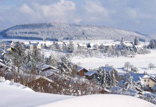 Snow-covered chalets and rolling hills in Holiday village Öfingen, Germany, pictured in a winter setting.