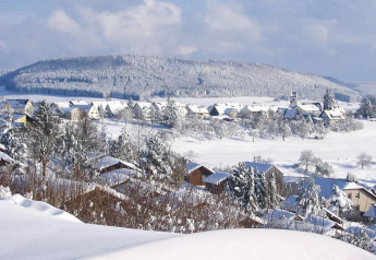 Snow-covered chalets and rolling hills in Holiday village Öfingen, Germany, pictured in a winter setting.