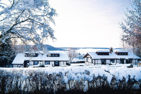 Chalets enneigés du village vacances Öfingen en Allemagne, entourés de paysage hivernal et de collines.