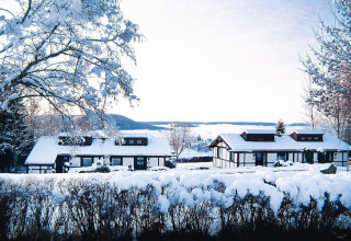 Chalets nevados en el Holiday village Öfingen, Alemania, rodeados de un paisaje invernal y colinas al fondo.
