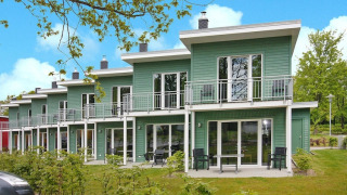 Grønne terrassehuse med balkon og havemøbler ved Ostseeresort Dampland på en solrig dag med blå himmel