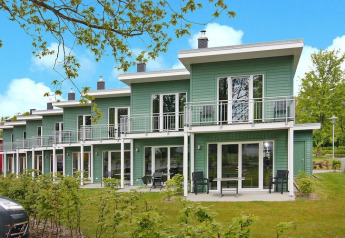 Casas adosadas verdes con balcones y muebles de jardín en Ostseeresort Dampland en un día soleado