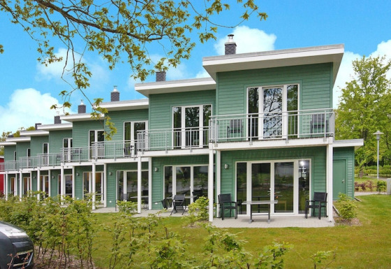 Grønne terrassehuse med balkon og havemøbler ved Ostseeresort Dampland på en solrig dag med blå himmel