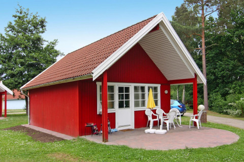 Rood huisje in Holiday park Markgrafenheide Warnemünde Type 1 met terras, witte stoelen en gele parasol.
