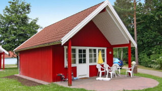 Casa rossa al Holiday park Markgrafenheide Warnemünde Tipo 1 con patio, sedie bianche e ombrellone giallo.