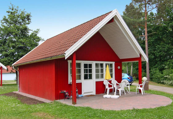 Red lodge at Holiday park Markgrafenheide Warnemünde Type 1 with patio, white chairs, and yellow umbrella.