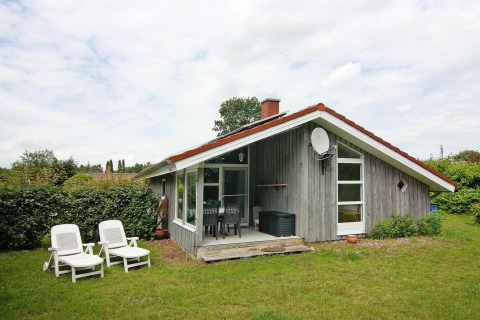Træhytte kaldet Holiday home in Hünning med rødt tag, grøn have og hvide havestole foran huset.