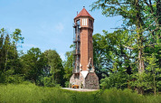 Joli chalet nommé « Water tower 75 sqm », en forme de tour, entouré de verdure en Allemagne.