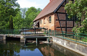 Imagen del chalet 'Water tower 75 sqm' junto a un canal, edificio de ladrillo y árboles verdes en Alemania.