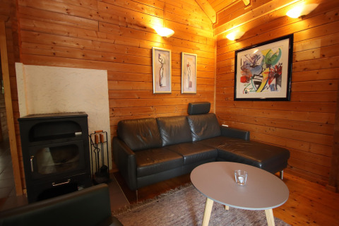 Træbeklædt stue i Holiday home Svenja Wiefelstede-Lehe, med sort sofa, brændeovn og kunstværker.