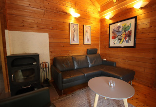 Træbeklædt stue i Holiday home Svenja Wiefelstede-Lehe, med sort sofa, brændeovn og kunstværker.