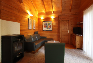 Living room with wooden walls, black sofa, fireplace, and wall art in Holiday home Svenja Wiefelstede-Lehe, Germany.