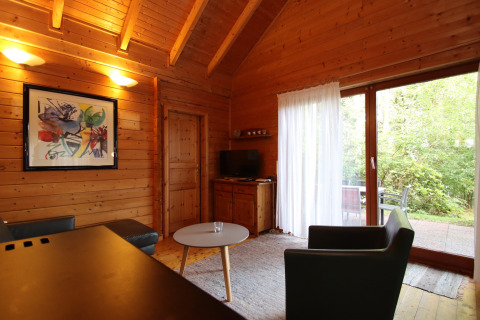 Acogedora sala de estar de madera con arte moderno, sillones, mesa de centro y vista al patio verde.