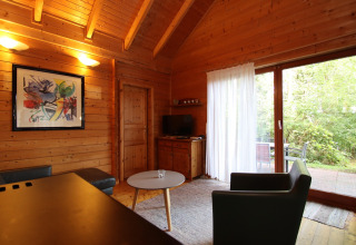 Cozy wooden living room with modern art on the wall, armchairs, coffee table and view of green patio.