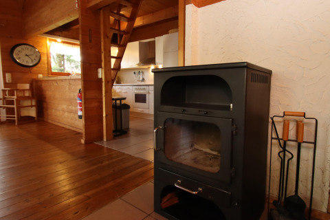Vista interior de una acogedora cabaña vacacional con estufa de leña, piso de madera y cocina en Alemania.