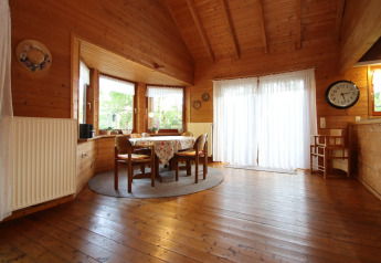 Acogedor comedor en una cabaña de madera con mesa redonda, sillas, ventanales y cortinas blancas.