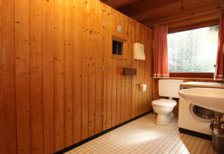 Badeværelse med træpaneler, toilet, vaskemaskine, håndvask og stort vindue i Holiday home Svenja.