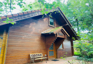 Houten lodge met schuin dak en bankje buiten, tussen bomen bij Holiday home Svenja in Duitsland.