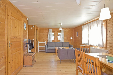 Woonkamer van houten lodge met grijze banken, eettafel en grote ramen in Type C House Duitsland.