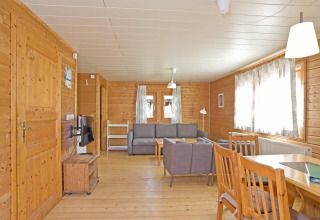 Woonkamer van houten lodge met grijze banken, eettafel en grote ramen in Type C House Duitsland.