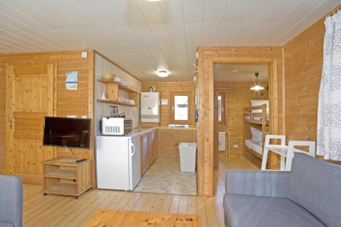 Interieur van Type C House lodge met houten wanden, keuken, stapelbedkamer en tv-woonhoek.