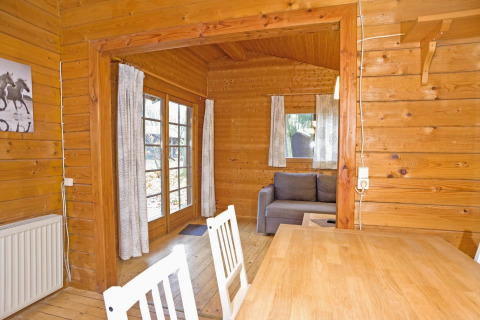 Wooden lodge interior in Germany featuring a dining table, chairs, sofa, and large curtained windows.