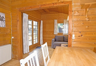 Wooden lodge interior in Germany featuring a dining table, chairs, sofa, and large curtained windows.